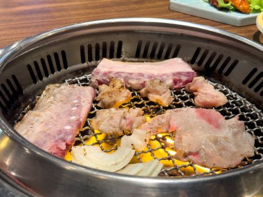 Grilling pork belly meat on a round iron BBQ net in restaurant for eating, fresh delicious food cuisine lifestyle.