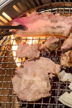 Grilling pork belly meat on a round iron BBQ net in restaurant for eating, fresh delicious food cuisine lifestyle.