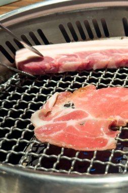 Grilling pork belly meat on a round iron BBQ net in restaurant for eating, fresh delicious food cuisine lifestyle.