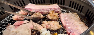 Grilling pork belly meat on a round iron BBQ net in restaurant for eating, fresh delicious food cuisine lifestyle.