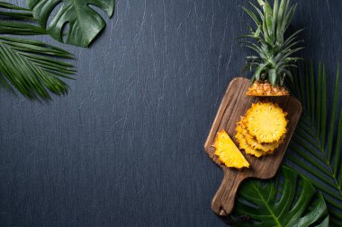 Koyu mavi arka planda tropikal yapraklı taze kesilmiş ananas manzarası.