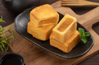 Lezzetli Tayvan usulü ananaslı pasta. Tahta bir masada tatlı. Arka planda sıcak çay var..