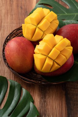 Taze olgun mango meyvelerinin en üst görüntüsü. Koyu ahşap masa arkasında yapraklar var..