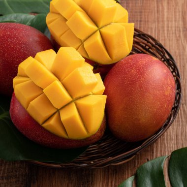 Mango. Taze olgun mango meyvelerini koyu ahşap masa zemininde yeşil yapraklarla kaplayın..