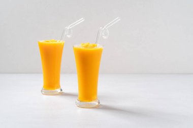 Taze nefis mango suyu. Smoothie soğuk içeceği cam bardakta gri masa arkasında cam pipetle yakın plan konsepti..