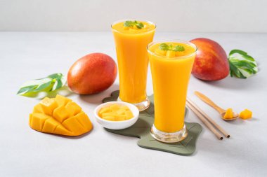 Taze nefis mango suyu. Smoothie soğuk içeceği cam bardakta gri masa arkasında cam pipetle yakın plan konsepti..