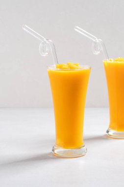 Taze nefis mango suyu. Smoothie soğuk içeceği cam bardakta gri masa arkasında cam pipetle yakın plan konsepti..