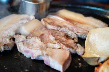 Jeju Kore restoranında kızarmış siyah domuz eti, demir tabakta taze Kore mutfağı marul, kimchi, banchan ve sos, yaşam tarzı.