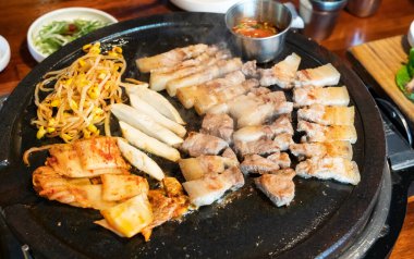 Jeju Kore restoranında kızarmış siyah domuz eti, demir tabakta taze Kore mutfağı marul, kimchi, banchan ve sos, yaşam tarzı.