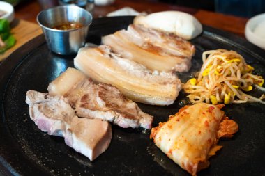 Jeju Kore restoranında kızarmış siyah domuz eti, demir tabakta taze Kore mutfağı marul, kimchi, banchan ve sos, yaşam tarzı.