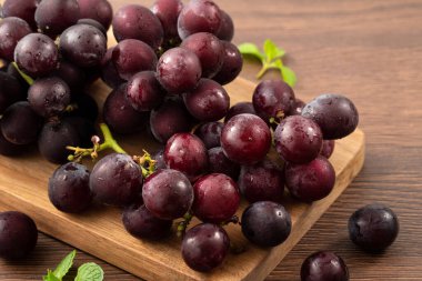 Ahşap masa arkasındaki tepside lezzetli bir demet mor üzüm meyvesi.