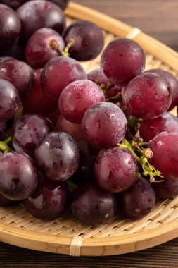Ahşap masa arkasındaki tepside lezzetli bir demet mor üzüm meyvesi.