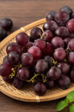Ahşap masa arkasındaki tepside lezzetli bir demet mor üzüm meyvesi.