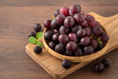 Ahşap masa arkasındaki tepside lezzetli bir demet mor üzüm meyvesi.