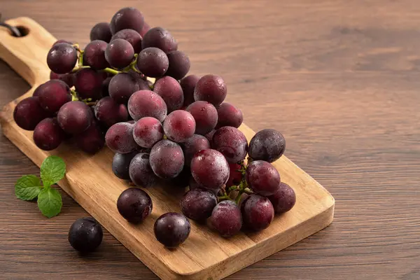 Ahşap masa arkasındaki tepside lezzetli bir demet mor üzüm meyvesi.