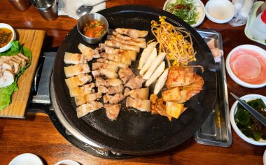 Jeju Kore restoranında kızarmış siyah domuz eti, demir tabakta taze Kore mutfağı marul, kimchi, banchan ve sos, yaşam tarzı.