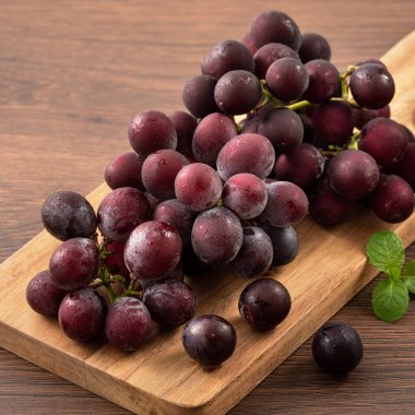 Ahşap masa arkasındaki tepside lezzetli bir demet mor üzüm meyvesi.