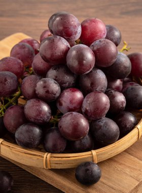 Ahşap masa arkasındaki tepside lezzetli bir demet mor üzüm meyvesi.