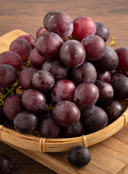 Ahşap masa arkasındaki tepside lezzetli bir demet mor üzüm meyvesi.