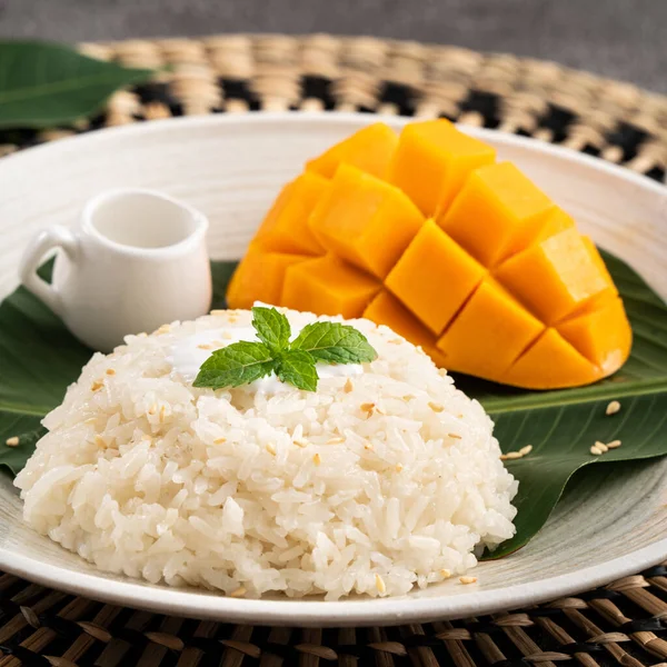 Delicious Thai mango sticky rice with cut fresh mango fruit in a plate on gray table background.