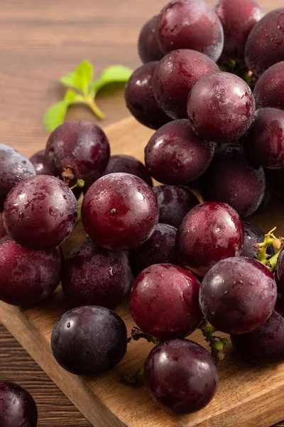 Ahşap masa arkasındaki tepside lezzetli bir demet mor üzüm meyvesi.