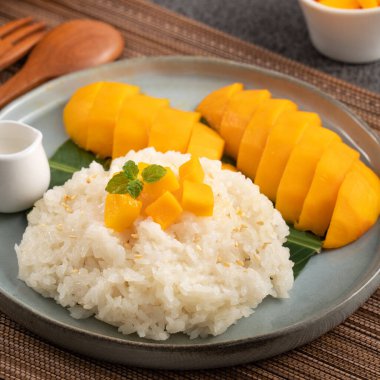 Lezzetli Tayland mangolu yapışkan pirinç ve gri masa arkasındaki tabakta taze mango meyvesi..