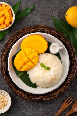 Lezzetli Tayland mangolu yapışkan pirinç ve gri masa arkasındaki tabakta taze mango meyvesi..