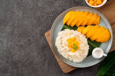 Lezzetli Tayland mangolu yapışkan pirinç ve gri masa arkasındaki tabakta taze mango meyvesi..