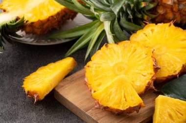 Koyu gri masa arkaplanının üzerinde taze kesilmiş sulu bir ananas..