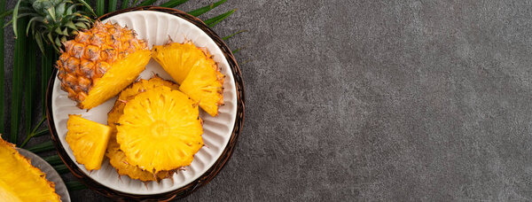 Top view of fresh cut pineapple with tropical leaves on dark gray table background.