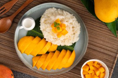 Lezzetli Tayland mangolu yapışkan pirinç ve gri masa arkasındaki tabakta taze mango meyvesi..