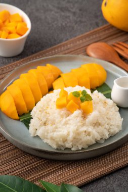 Lezzetli Tayland mangolu yapışkan pirinç ve gri masa arkasındaki tabakta taze mango meyvesi..