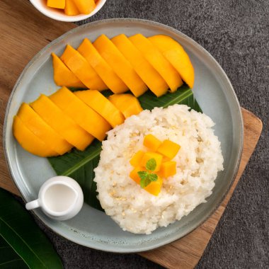 Lezzetli Tayland mangolu yapışkan pirinç ve gri masa arkasındaki tabakta taze mango meyvesi..