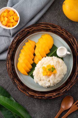 Lezzetli Tayland mangolu yapışkan pirinç ve gri masa arkasındaki tabakta taze mango meyvesi..