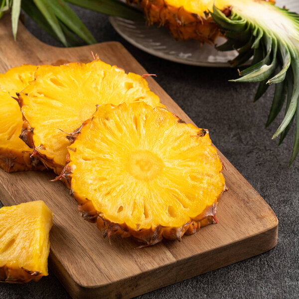 Fresh cut sliced juicy pineapple in a plate over dark gray table background.