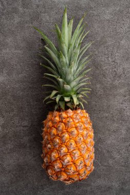 Koyu gri masa arkaplanında tropikal yapraklı taze ananas manzarası.