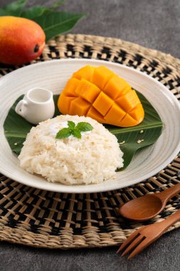 Lezzetli Tayland mangolu yapışkan pirinç ve gri masa arkasındaki tabakta taze mango meyvesi..