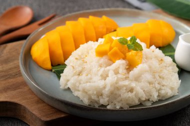 Lezzetli Tayland mangolu yapışkan pirinç ve gri masa arkasındaki tabakta taze mango meyvesi..
