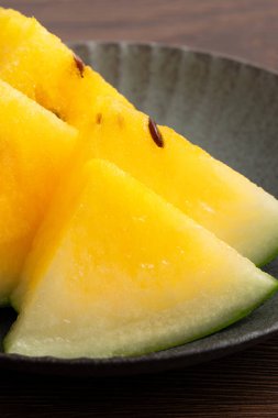 Sliced yellow golden watermelon in a plate on wooden table background ready for eating.