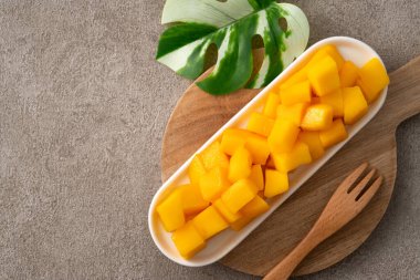 Gri masa zemininde taze doğranmış mango küpleri ve tropikal yaprak yemek için..