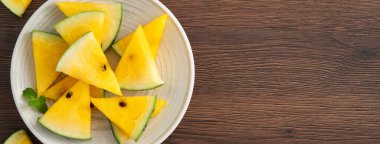 Dilimlenmiş sarı karpuz desenli düz tahta masa arkasında yatıyordu..