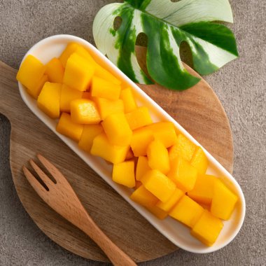 Gri masa zemininde taze doğranmış mango küpleri ve tropikal yaprak yemek için..