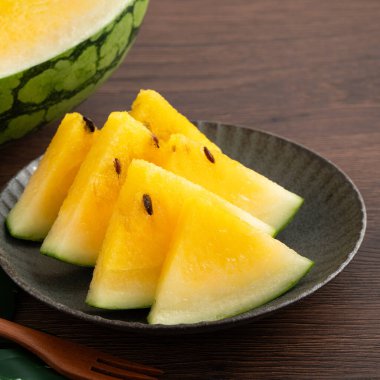 Sliced yellow golden watermelon in a plate on wooden table background ready for eating.