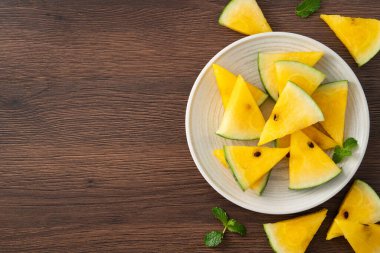 Dilimlenmiş sarı karpuz desenli düz tahta masa arkasında yatıyordu..