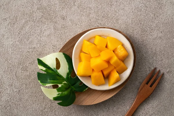 stock image Fresh chopped, diced mango cubes on gray table background with tropical leaf for eating.