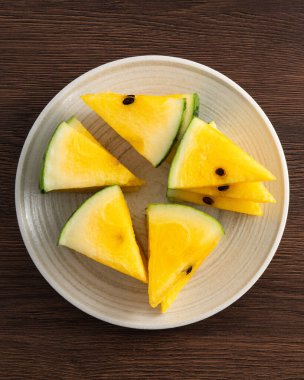 Dilimlenmiş sarı karpuz desenli düz tahta masa arkasında yatıyordu..