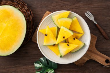 Dilimlenmiş sarı karpuz desenli düz tahta masa arkasında yatıyordu..