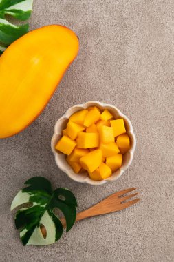 Gri masa zemininde taze doğranmış mango küpleri ve tropikal yaprak yemek için..