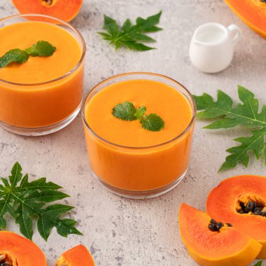 Tropikal meyve tasarımı konsepti için gri masa zemininde cam bardakta taze, lezzetli papaya sütü..