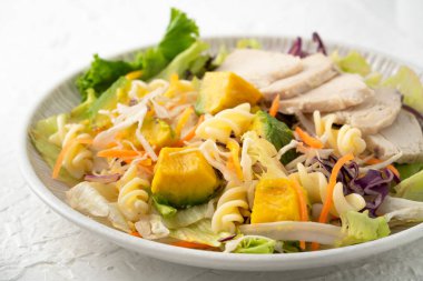 Taze avokado marul salatası kasesi dilimlenmiş tavuk eti ve Rotini beyaz masa arkasında bir tabakta.